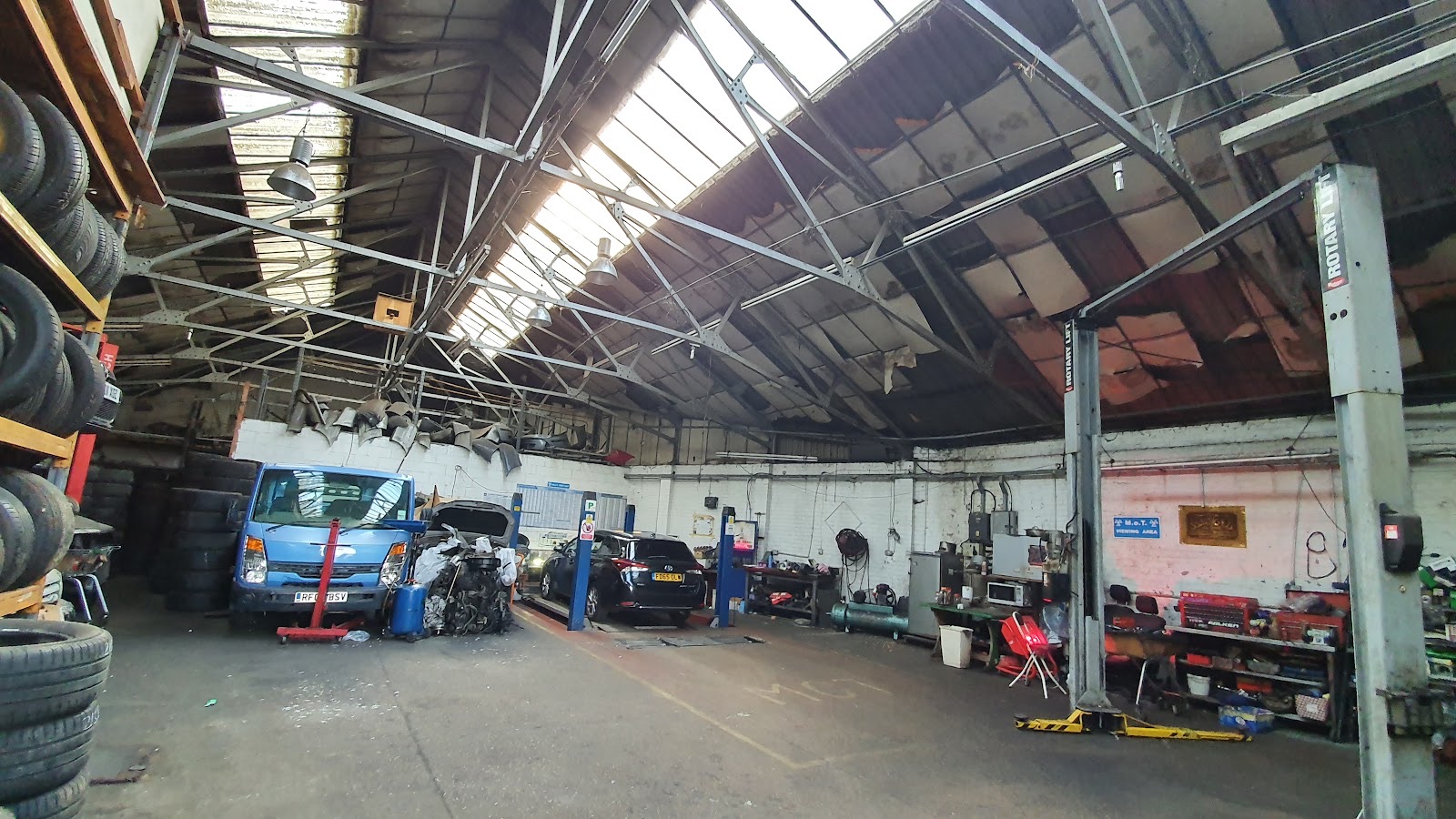 A white Rolls-Royce raised on the ramp inside 1 Stop MOT & repairs ltd on , under the workshop sign
